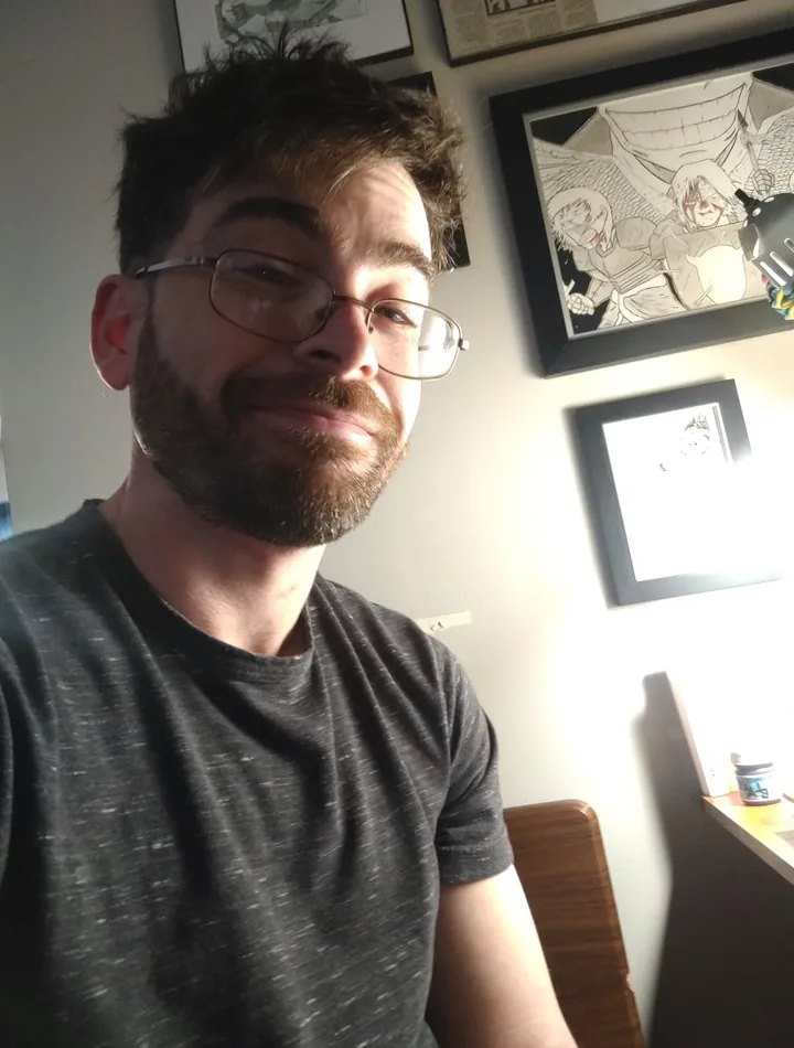 Nick Daulton at home, framed drawings on the wall behind him.
